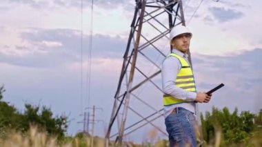 Bir tasarımcı yüksek voltaj kulesini kontrol eder. Bir güç iletim pilonuna hizmet eden kasklı bir mühendis. Güç hattında kask takan bir elektrik mühendisi. Bir tasarımcı yüksek voltaj sensörünü kontrol eder