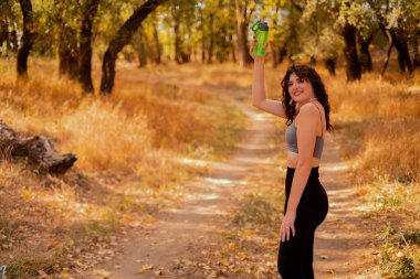 Genç kadın parkta egzersiz yaparken su içer, sağlıklı yaşam tarzı konsepti, doğa ile yalnızlık, sonbahar parkı, ormanda sabah koşusu