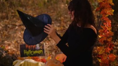 Elinde balkabağı feneri olan cadı bir kız ormanın arka planında poz veriyor. Korkunç suratlı Cadılar Bayramı balkabağı. Cadı kostümü giymiş genç bir kadın. Cadılar Bayramı konsepti Elini sallıyor..