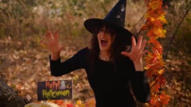 Elinde balkabağı feneri olan cadı bir kız ormanın arka planında poz veriyor. Korkunç suratlı Cadılar Bayramı balkabağı. Cadı kostümü giymiş genç bir kadın. Cadılar Bayramı konsepti Elini sallıyor..