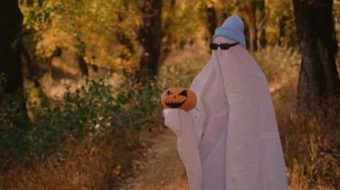 İyi küçük hayalet. Cadılar Bayramı Partisi. Sonbahar ormanındaki hayalet kostümüne benzeyen yarıklı çarşaflı bir çocuğun elinde bir balkabağı tutması korkutucu ve korkutucudur.