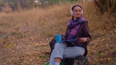 Sırt çantalı bir kadın, kahverengi bir kazak giymiş, elinde bir harita tutan, sonbahar ormanlarında güneşli havanın tadını çıkaran, uçurumun kenarında seyahat eden, 