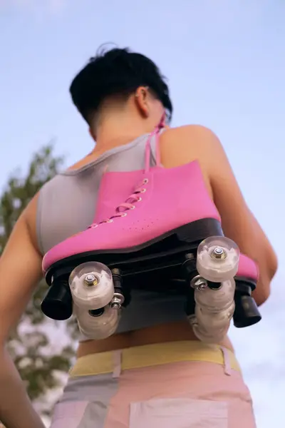 sporty woman view from back, posing with a pair of roller skates on her shoulder, smiling and looking to the side, sport lifestyle concept, copy space