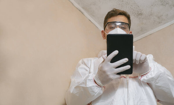 Человек, смотрящий на затхлую белую стену. Делает заметки об уборке на телефоне. Специалист санитарно-эпидемиологической службы.
