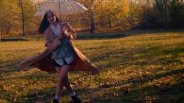 Sonbahar parkında şemsiyeyle dönen bir kız. Renkli yapraklı neşeli sonbahar sahnesi, yağmur koruması, şeffaf şemsiye, hava tahmini