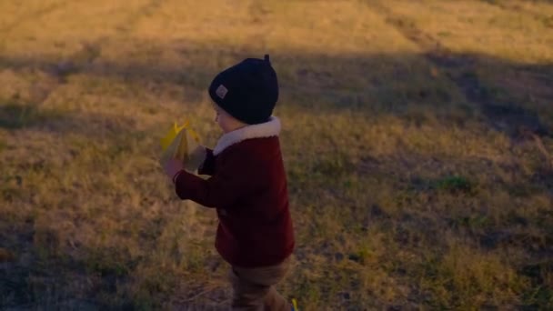 秋の服を着た少年が紙飛行機で遊び 空中に投げ込んだ 秋の季節の楽しいアウトドアアクティビティ 創造性と楽しさを育む — ストック動画