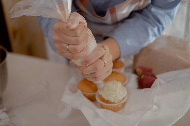 Keklerin üzerine krema döken, ev yapımı pişirilmiş ürünlerini sergileyen kadın bir pasta şefi. Ev yapımı ve küçük ölçekli işletmelerin çekiciliğini işindeki yetenekli bir fırıncı imajıyla keşfedin..