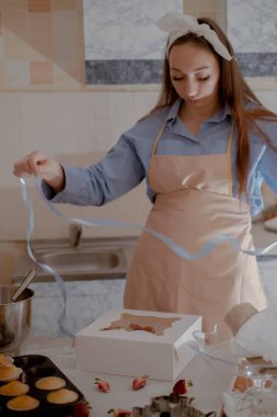 Dişi bir pasta şefi, müşterilere gönderilmek üzere paketlemek için kek paketliyor, ev yapımı pişirme sergiliyor. Glütensiz ve şekersiz ürünlerle küçük ölçekli, çevre dostu pişirmenin özünü tecrübe edin, sağlıklı beslenmeyi teşvik edin..