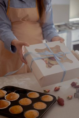 Dişi bir pasta şefi, müşterilere gönderilmek üzere paketlemek için kek paketliyor, ev yapımı pişirme sergiliyor. Glütensiz ve şekersiz ürünlerle küçük ölçekli, çevre dostu pişirmenin özünü tecrübe edin, sağlıklı beslenmeyi teşvik edin..