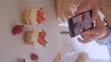 Bir kadın pasta şefi, web sitesinin reklamını yapmak için cep telefonuyla fotoğraf çekiyor, ev yapımı pişirme sergiliyor. Glütensiz ve şekersiz ürünlerle küçük ölçekli, çevre dostu üretim deneyimi