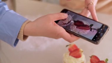Bir kadın pasta şefi, web sitesinin reklamını yapmak için cep telefonuyla fotoğraf çekiyor, ev yapımı pişirme sergiliyor. Glütensiz ve şekersiz ürünlerle küçük ölçekli, çevre dostu üretim deneyimi