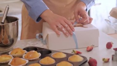 Bir kadın pasta şefi bir kutuya kek paketliyor. Ev yapımı, küçük işletme, çevre dostu üretim, glütensiz, şekersiz, sağlıklı yeme alışkanlıklarını teşvik eden.