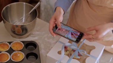Bir kadın pasta şefi, web sitesinin reklamını yapmak için cep telefonuyla fotoğraf çekiyor, ev yapımı pişirme sergiliyor. Glütensiz ve şekersiz ürünlerle küçük ölçekli, çevre dostu üretim deneyimi