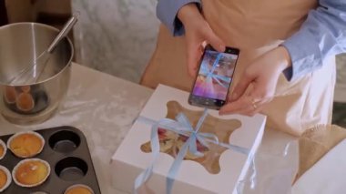 Bir kadın pasta şefi, web sitesinin reklamını yapmak için cep telefonuyla fotoğraf çekiyor, ev yapımı pişirme sergiliyor. Glütensiz ve şekersiz ürünlerle küçük ölçekli, çevre dostu üretim deneyimi