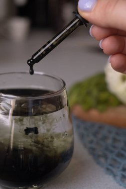Bir kadının eli bardağa sıvı klorofil döker, sağlıklı bir yaşam tarzı, vitamin eksikliği, kansızlık ve sabah ritüelleri için vitaminleri teşvik eder..