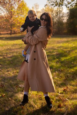 Bir anne ve oğul bahar parkında oynuyorlar, anne çocuğu döndürüyor ve her ikisi de gülümsüyor. Anne sevgisi ve sıcaklıkla dolu bir aile günü..