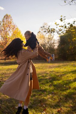 Bir anne ve oğul bahar parkında oynuyorlar, anne çocuğu döndürüyor ve her ikisi de gülümsüyor. Anne sevgisi ve sıcaklıkla dolu bir aile günü..