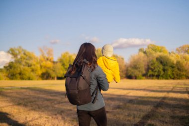 Sırt çantalı bir kadın oğluyla seyahat ediyor, ormanda bir aile gezisinin tadını çıkarıyor. Aktif bir yaşam tarzını, spor malzemelerini ve çevre dostu turizmi benimsiyorlar..
