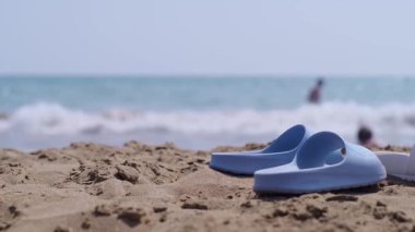 Sahilde sandaletler, kumsala vuran dalgalar, plaj ayakkabıları ve aksesuarları, turistik tatil beldeleri ve plajlar..