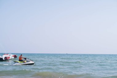 Can yeleği giymiş bir adam, ekstrem sporları ve rehberli turları temsil eden bir jet ski kullanıyor. Turizm hizmetleriyle adrenalin dolu maceralar yaşayın..