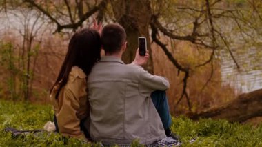 Bir kız ve bir adam parkta dolaşırken akıllı telefonlarıyla selfie çekiyorlar. Turizm hizmetleri ve seyahat, turist fotoğrafçılığı ve fotoğraf turları, göl kenarı otelleri ve tatil beldeleri.