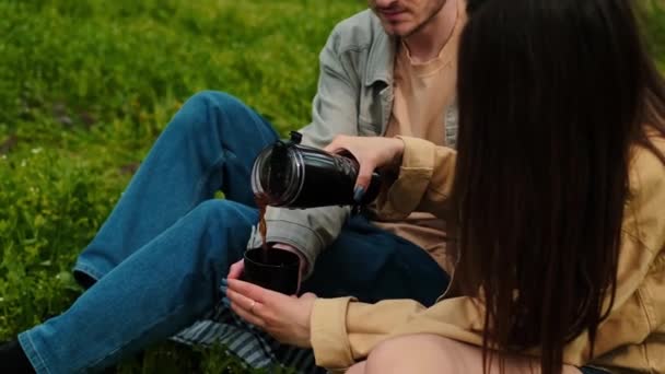 一个女孩把热茶从热水瓶里倒入一杯给她的伴侣喝 用热饮料在大自然中露营 露营用具 运动服和鞋袜 积极的休闲和旅游路线 — 图库视频影像