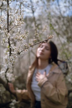 Bir kadın bahçede çiçek açan bir ağacın yanında duruyor. Botanik bahçesinde ve parkta gezinmek, doğanın ortasındaki doğal güzelliği ve tazeliği kucaklamak..