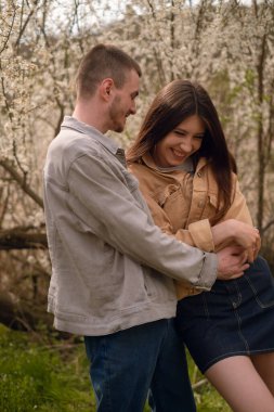 Genç bir çift çiçek açan bahçede yürüyor ve gülüyor. Botanik bahçesinde ve parkta dolaşmak, aile toplantılarının ve etkinliklerin tadını çıkarmak. Sevgililer Günü