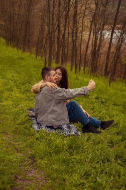 Bir adam ve bir kız ormanda piknik yaparken telefonlarında selfie çekiyorlar, doğada romantik bir buluşma yakalıyorlar..