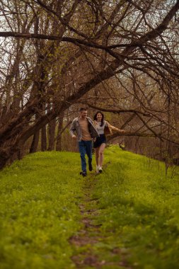 Genç bir çift orman yolunda koşuyor, Sevgililer Günü 'nde doğa yürüyüşünün tadını çıkarıyorlar.