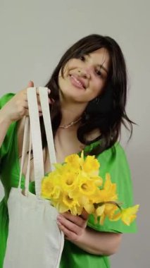 Bir kadın içinde buket, içinde sarı nergis olan bir çanta taşıyor. Kutlamalar için eve çiçek getiriyor. Romantik ve şenlikli anları vurguluyor..