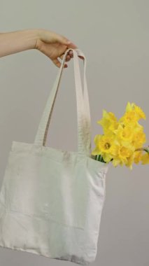 İçinde çiçek buketi olan beyaz alışveriş torbası, gri arka planda tutulan kız, bahar tatili konsepti, 8 Mart ve Anneler Günü..