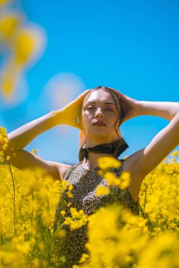 Esmer kız çiçek açan sarı tarlada duruyor, doğal güzelliğin tadını çıkarıyor, bitki malzemesi üretiyor, çiçek açıyor ve parfüm yapımında koku alıyor..