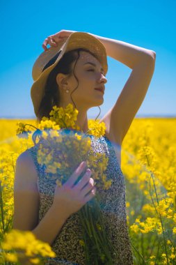 Çiçek buketli kadın, arka planda çiçek açan sarı kolza tohumu tarlası. Çiçek şirketlerinin konsepti, çiçek teslimatı ve doğanın güzelliğinin takdir edilmesi..