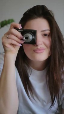 Kadın kendini klasik fotoğraf makinesiyle çekiyor, kendi fotoğrafçılığını kucaklıyor. Antika kameraları veya antika tasarımlı modern meslektaşlarını teşvik eder, nostalji ve benzersizliği vurgular.