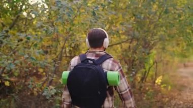 Sırt çantalı bir turist, kahverengi ekose gömlek ve kulaklık takarak kameradan uzaklaşır ve bir çeşit meditasyon olarak doğanın müziğini dinler..