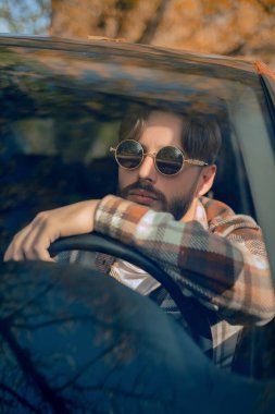 Arabanın ön camından bak: Gözlüklü, kareli gömlekli, yola odaklanmış, sabah işe koşan bir adam..