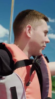 Kafkasyalı bir adam katamaranın direksiyonunu tutar, can yeleği giyer, doğanın ve manzaranın tadını çıkarır..