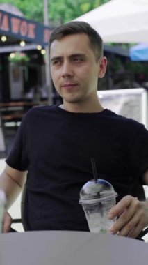 Beyaz adam serinletici bir kokteyl içiyor, açık hava kahvesi içiyor, soğuk içeceklerin tadını çıkarıyor. sstkDikey