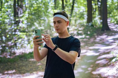 Elinde telefon tutan bir erkek sporcu, spor istatistiklerini kontrol ediyor. Spor performansı için teknoloji kullanılıyor.