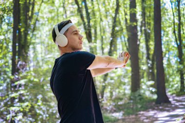 Kulaklıklı genç bir beyaz adam meditasyon müziği dinliyor, parkta koşudan önce ısınıyor..