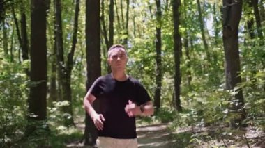 Orman ortamında eğitim programı yürütüyor. Bir adam parkta koşuyor, kameraya gülümsüyor, doğanın sükuneti ve huzurunun tadını çıkarıyor..