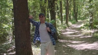Sırt çantalı bir erkek yürüyüşçü ormanda duruyor, yukarı bakıyor ve doğanın seslerinden ve dışarıdaki sükunetten zevk alıyor.