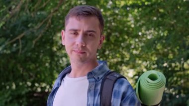 Sırt çantalı turist yoğun yeşil ormanda duruyor, kameraya gülümsüyor, doğanın ve maceranın tadını çıkarıyor..