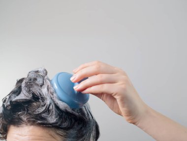 Duşta kafa derisi fırçası, kafasının üstünde koyu saçlı kızlar, kalın şampuan köpüğü, saç fırçasıyla kafa derisine masaj..