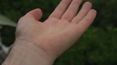 Yağmur damlası insan elinin üzerine düşer, arka planda yeşil doğa, çevresel restorasyon