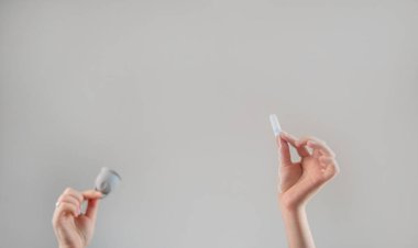 Bir kadın bir elinde tampon, diğer elinde regl bardağı tutarken, aybaşı bakımı için her birinin faydalarını karşılaştırıyor..