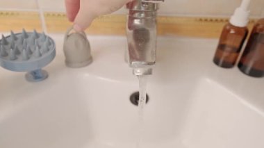 Dişi eller, metal bir musluktan akan suyun altında pembe bir adet bardağını yıkıyor. Adet sırasında alternatif hijyen kavramı