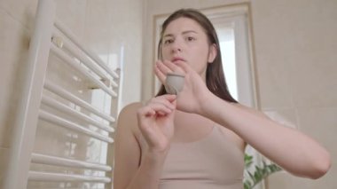 Bir kadın, regl bardağını tutar, onun güvenliği ve rahatlığı hakkındaki deneyimini paylaşır, özel hijyen için regl bardaklarını teşvik eder..