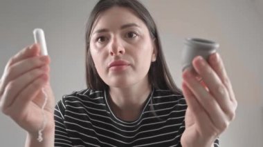 Bir kadın banyoda elinde tampon, diğer elinde regl bardağı tutarak kadın hijyen seçimini sembolize ediyor..